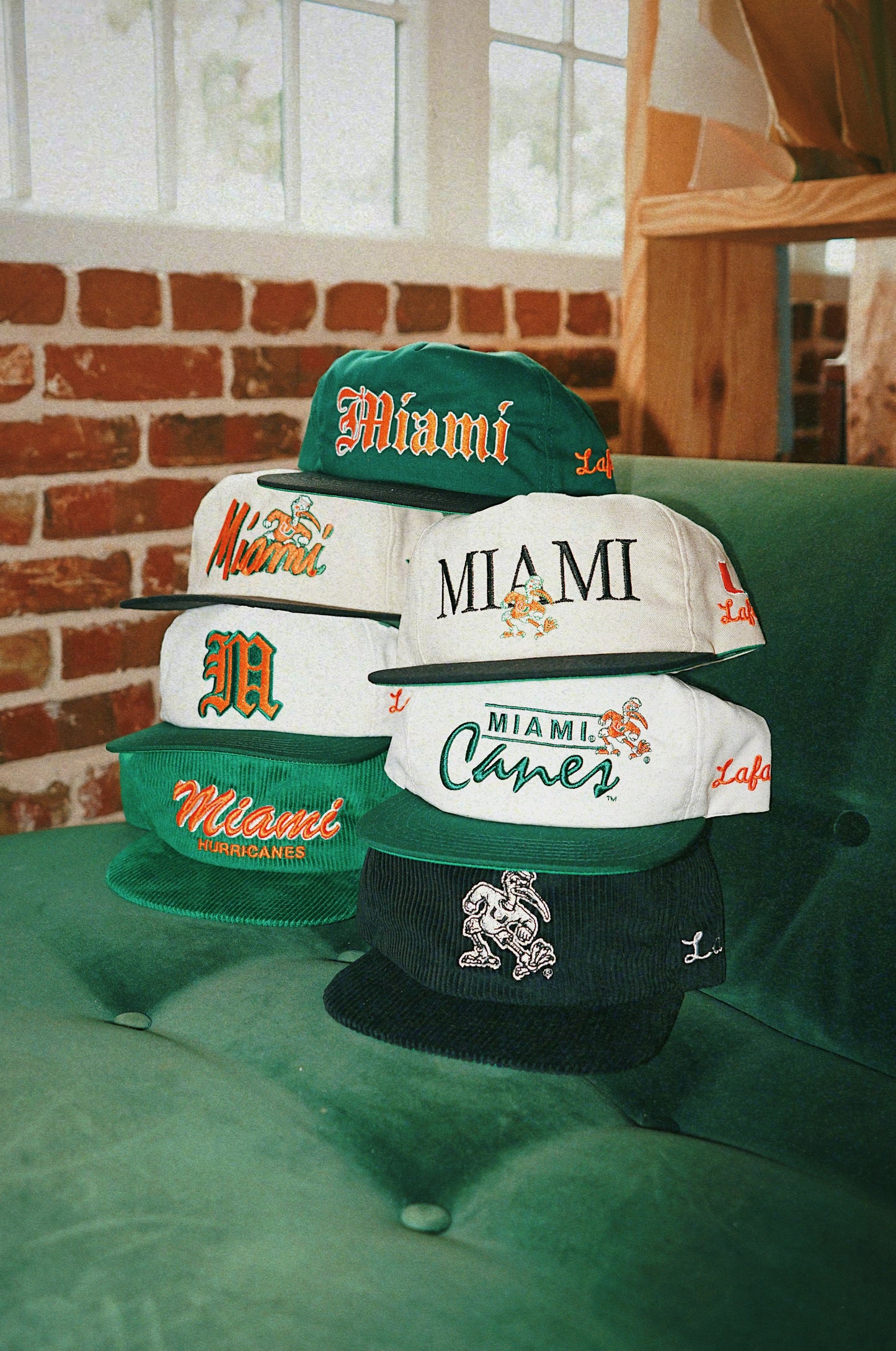 Collection of Miami-themed hats on a green surface with a brick wall background