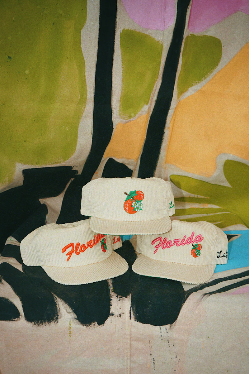 Three white caps with 'Florida' and orange design on a colorful floral-patterned couch.
