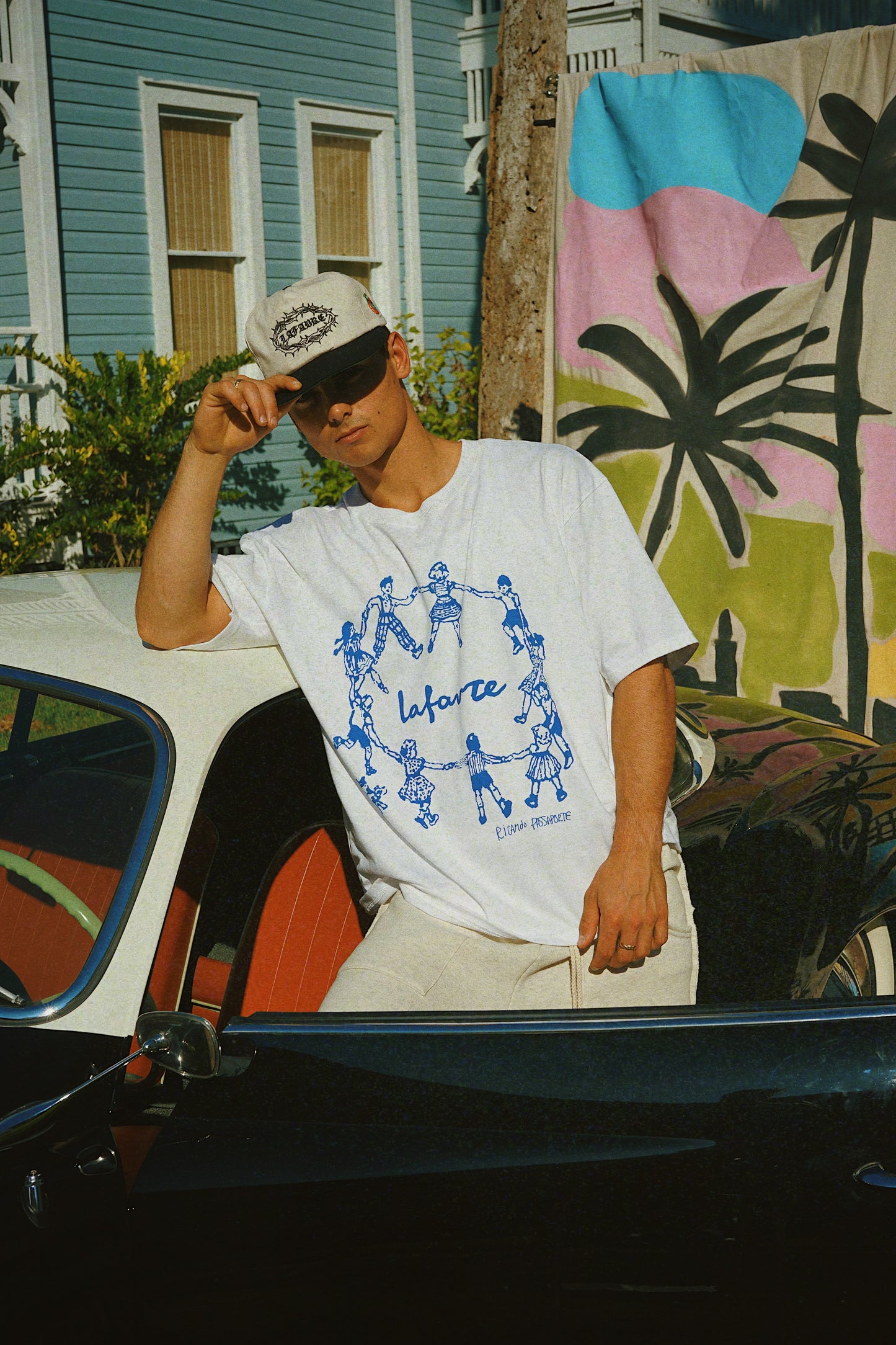 Person wearing a white t-shirt with blue graphics and text, standing in front of a colorful mural.