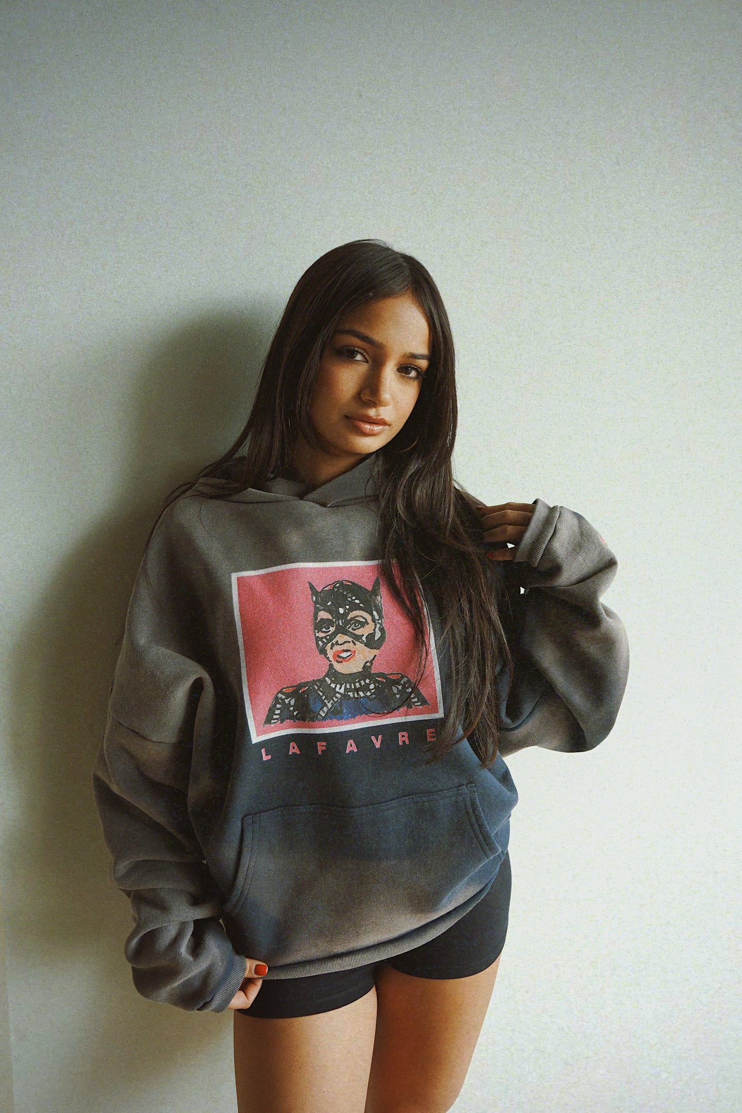 Person wearing a gray hoodie with a graphic design on a plain background