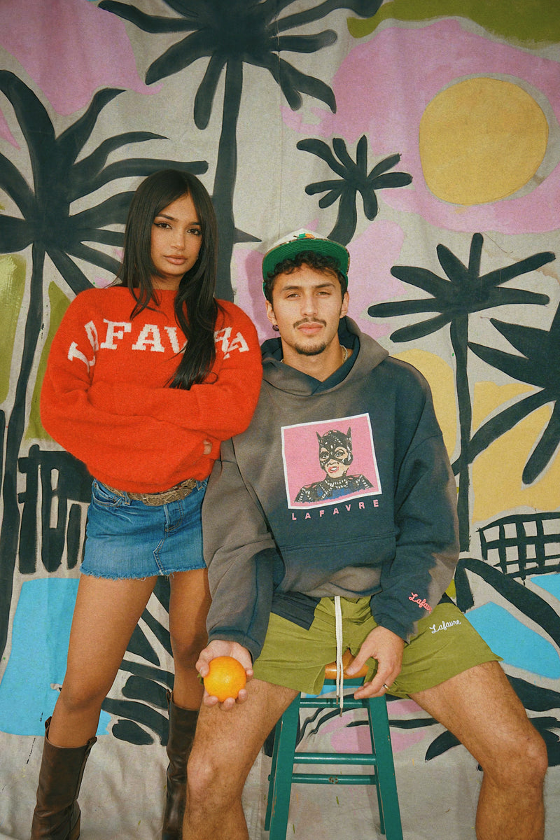Two people wearing colorful outfits in front of a vibrant, abstract wall.