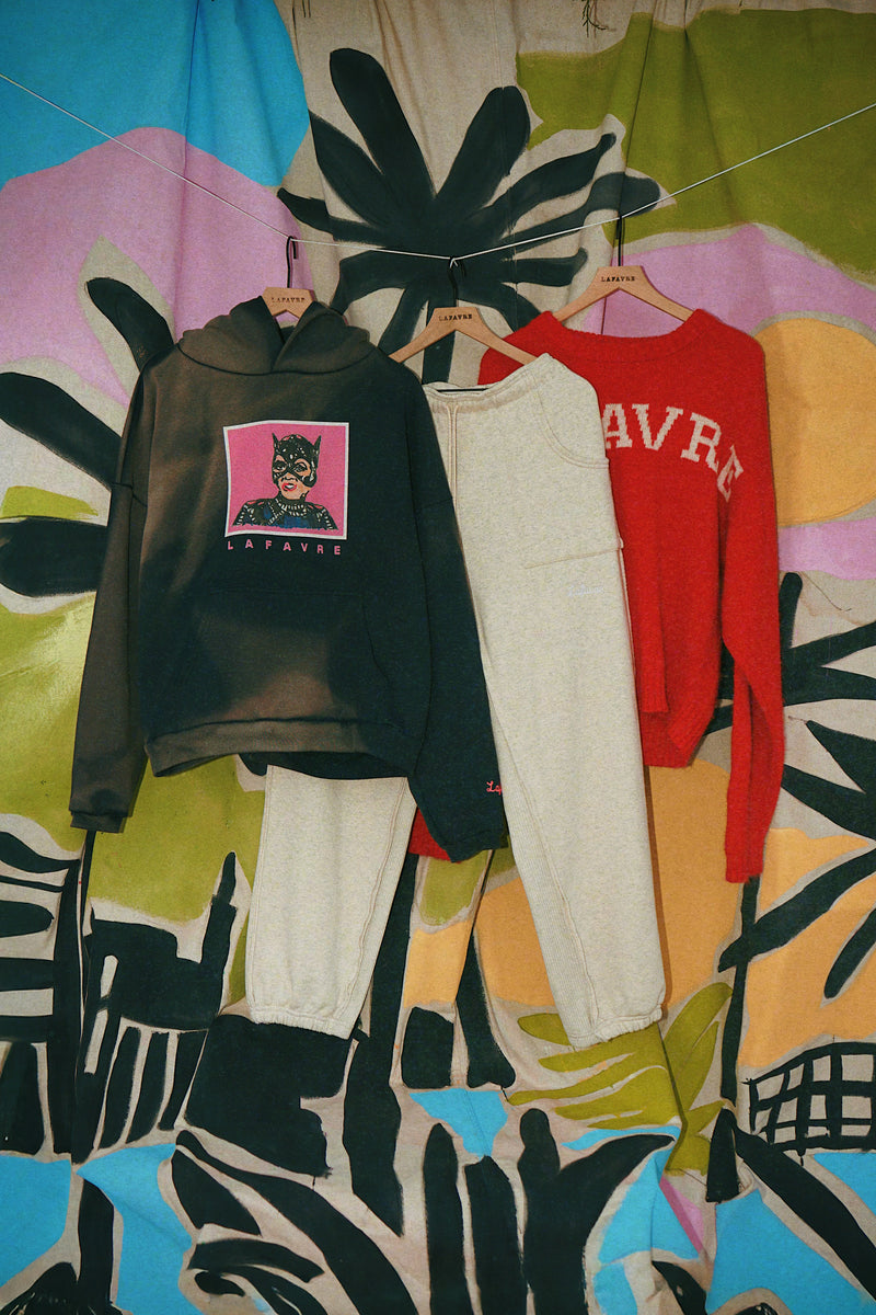 Clothing items including a hoodie, pants, and sweater hanging against a colorful abstract background.
