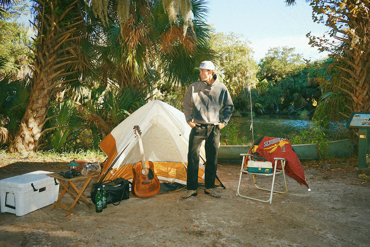 Person standing next to a tent with camping gear in a natural setting
