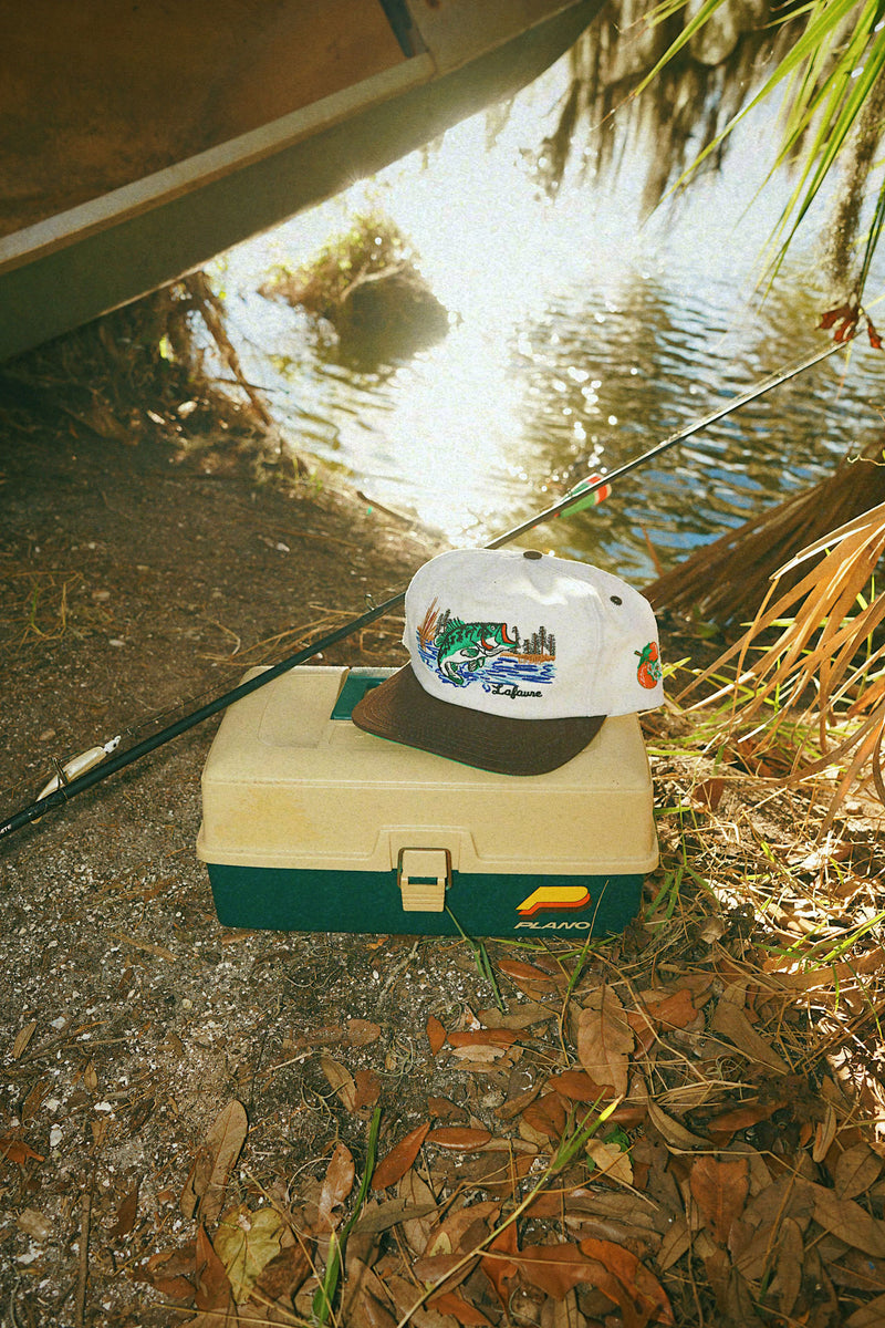 Lafavre bass hat and tackle box on a riverbank with fishing rod