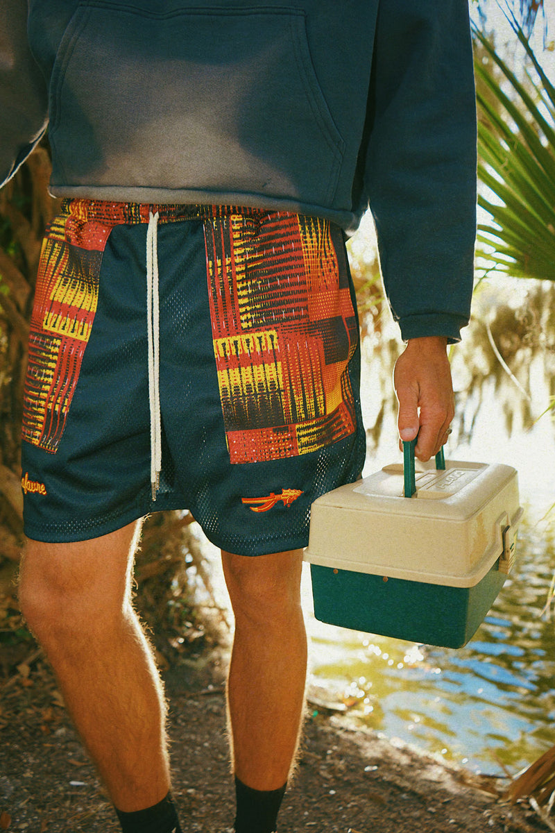 Person wearing fire mesh shorts holding a tackle box outdoors