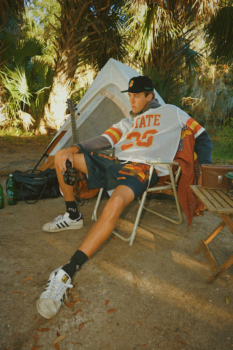 Person sitting outdoors wearing the Lafavre FSU capsule near a tent with palm trees in the background