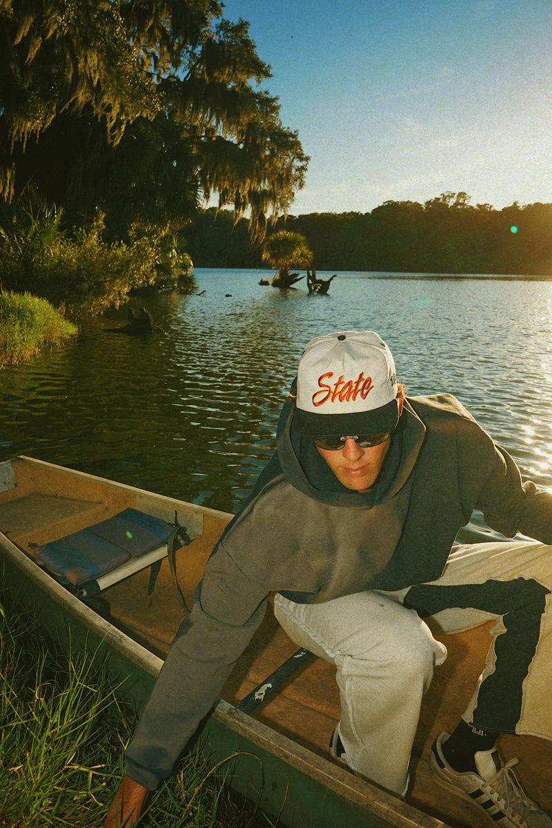 Person sitting in a boat on a lake wearing a 'State' cap